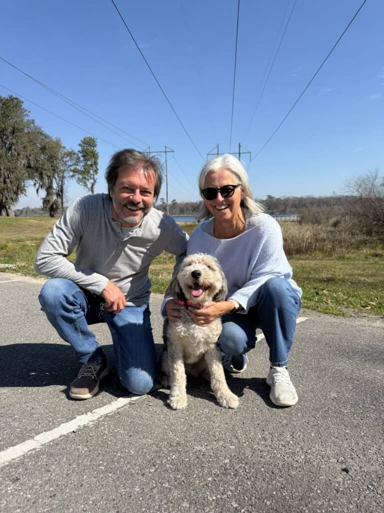 Forget Me Not Dog Training - A man and woman squatting on a road with a small puppy between them. They're outdoors under a clear sky with power lines and trees in the background.